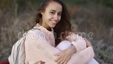 一个穿着针织<strong>粉色</strong>毛衣的漂亮女孩的特写，小背包坐在Autamn森林的<strong>毯</strong>子上。
